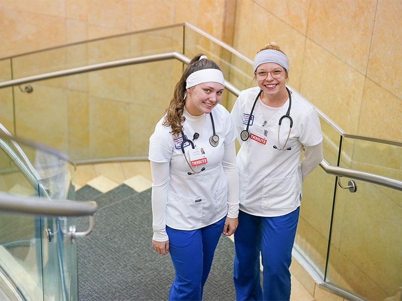 Two nursing students in scrubs smiling